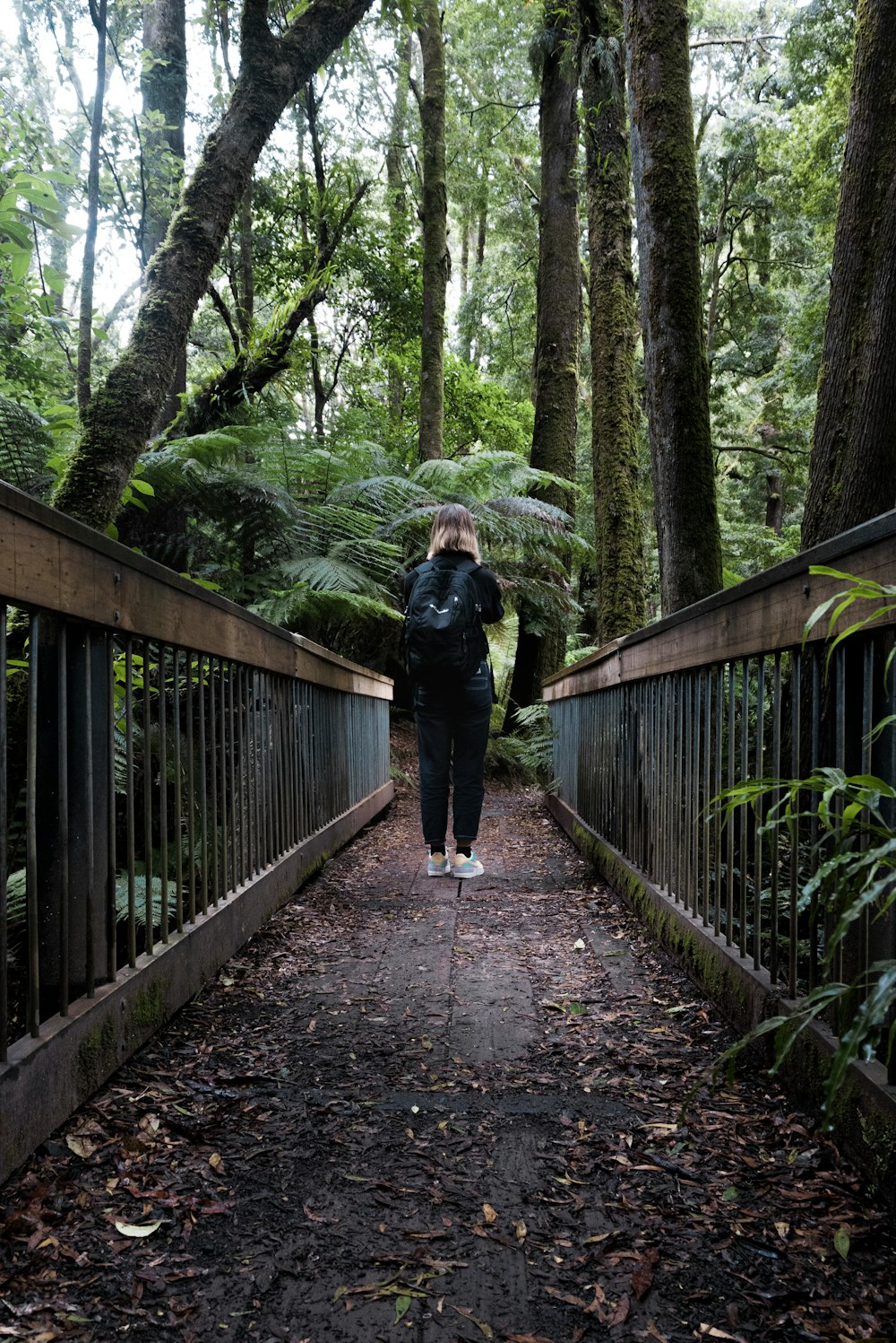 woman in black jacket and black pants walking on wooden bridge