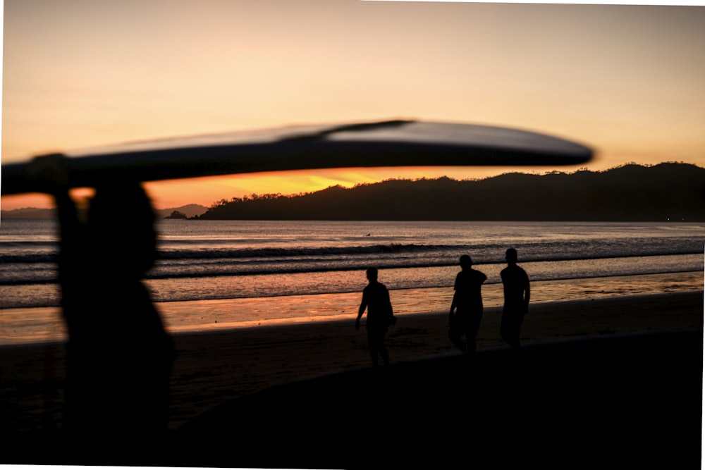 silhouette of 3 people standing on seashore during sunset