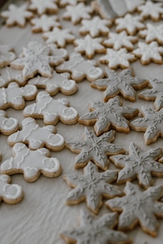 An assortment of intricately decorated cookies featuring snowflakes and gingerbread figures with white and gray icing, arranged on a light-colored surface.