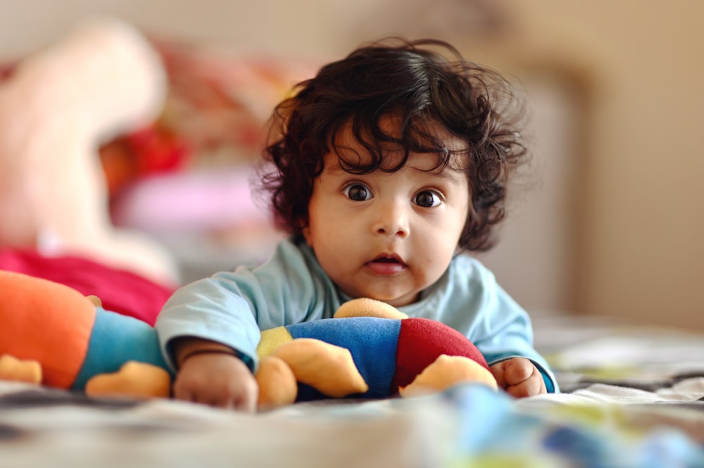 child in blue long sleeve shirt lying on bed