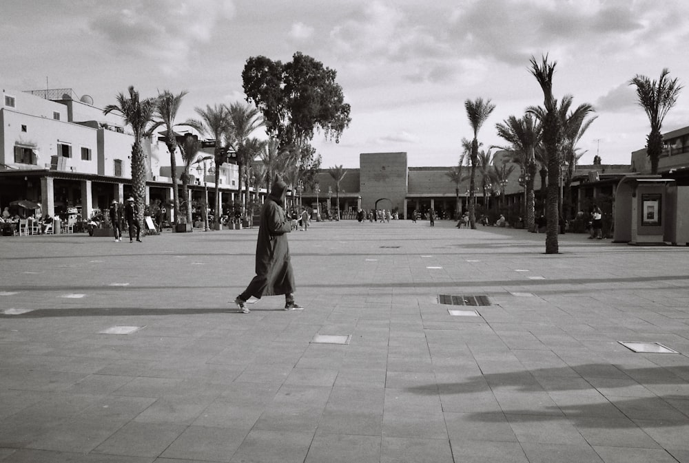 grayscale photo of woman walking on sidewalk near palm trees