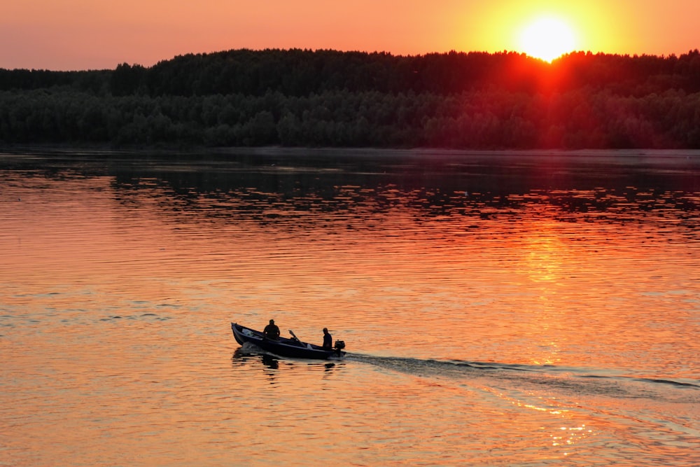 2 personas montando en bote en el cuerpo de agua durante la puesta del sol