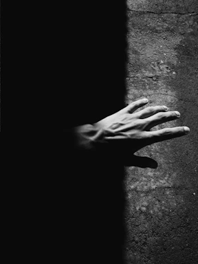 A stark black-and-white photo of a hand reaching out against a textured concrete wall, capturing raw emotion and connection.
