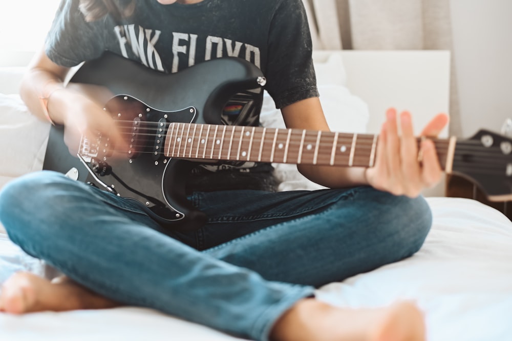 Hombre con camiseta de cuello redondo blanco y negro y jeans de mezclilla azules tocando la guitarra eléctrica