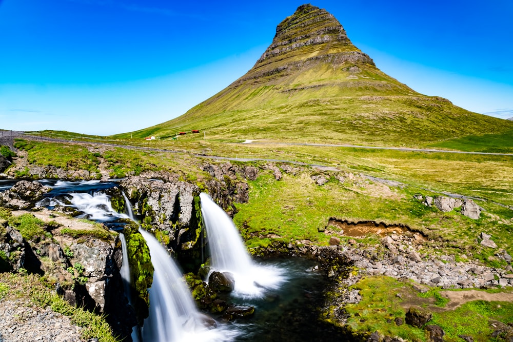 waterfalls on green grass field near brown mountain under blue sky during daytime