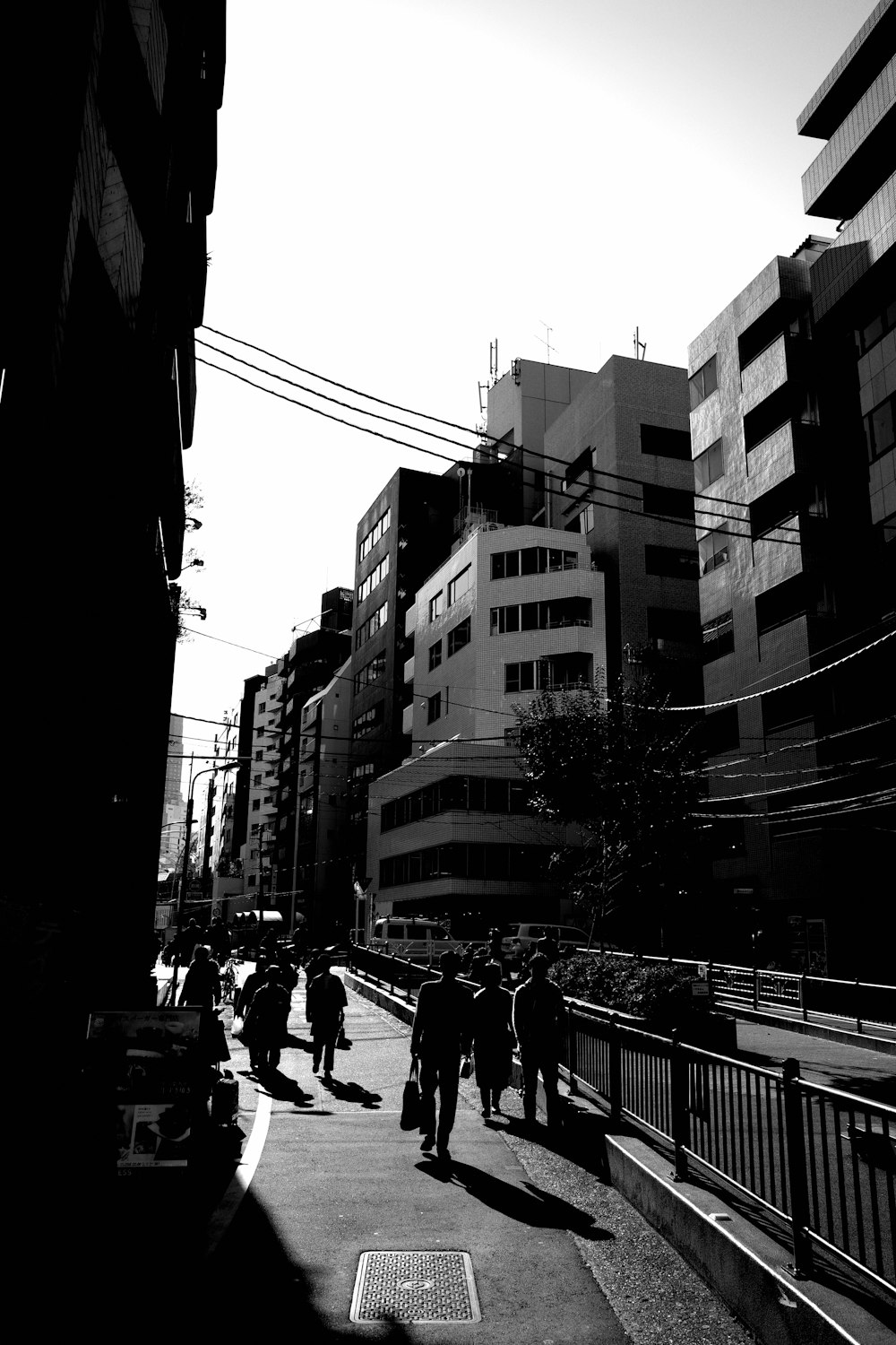 grayscale photo of people walking on street between buildings