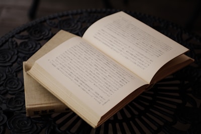Close-up of hands holding an open book with Japanese calligraphy on a wooden table.