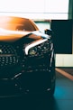 A close-up of a sleek, modern car with sharp headlights and a glossy finish. The vehicle is positioned indoors with soft lighting highlighting its contours. The photo emphasizes the car's luxurious design and high-quality details.