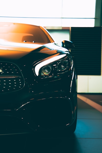 A close-up of a sleek, modern car with sharp headlights and a glossy finish. The vehicle is positioned indoors with soft lighting highlighting its contours. The photo emphasizes the car's luxurious design and high-quality details.