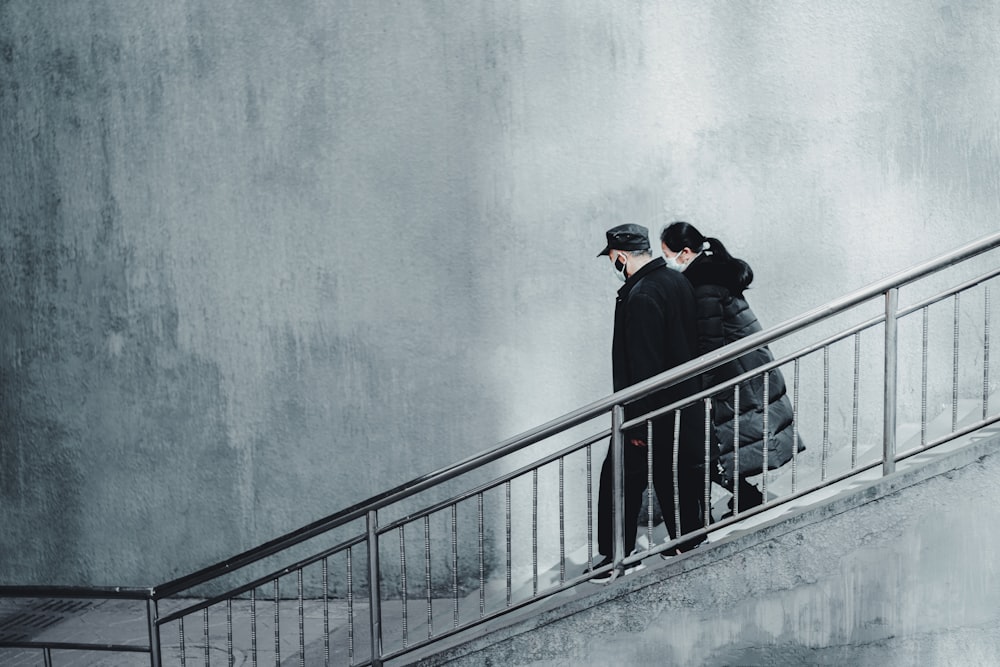 man in black jacket and black cap standing on gray concrete staircase