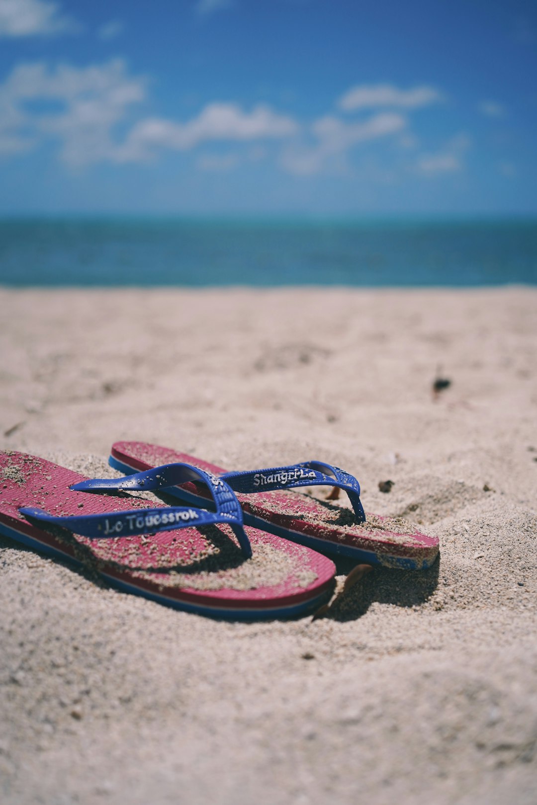 red and blue flip flops on white sand during daytime
