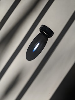 Close-up of a sleek black smart ring glowing with electric violet light on a minimalist white surface.