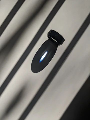 Close-up of a sleek, contemporary ring resting on a textured black surface with soft natural light highlighting its polished finish.