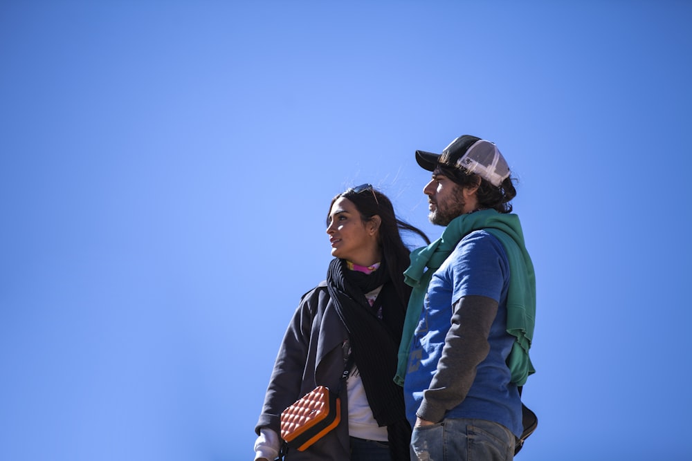 man in black jacket and blue denim jeans standing beside woman in green jacket