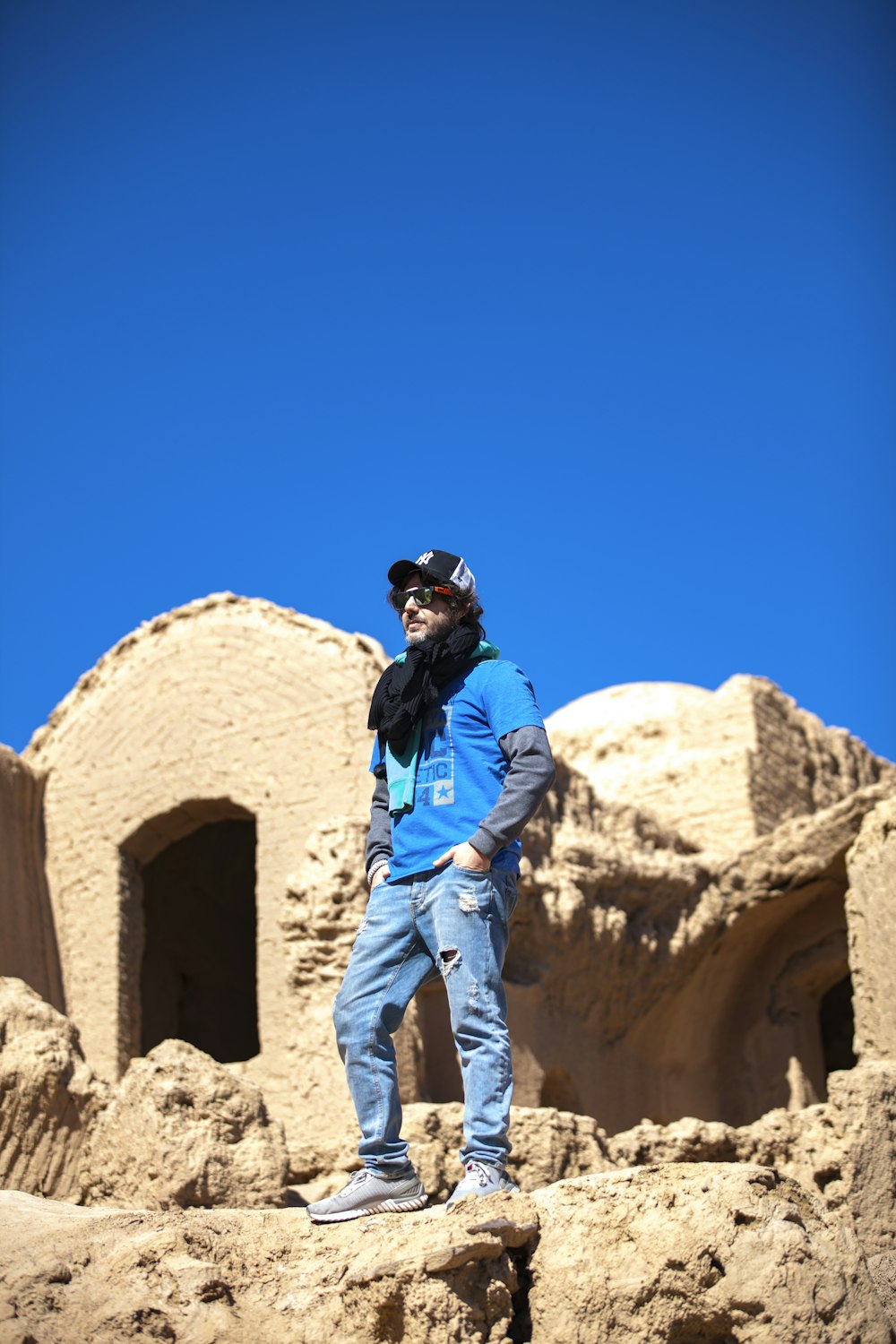 man in blue jacket and gray pants standing on brown rock formation during daytime