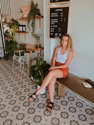 A chic woman in a light beige outfit sipping coffee in a sunlit minimalist cafe.