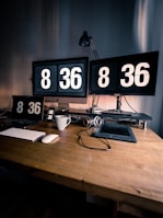The clock placed on a wooden desk beside a laptop and a coffee cup, highlighting its dual-purpose design.