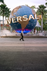 man in black jacket walking on sidewalk with blue and yellow heart shaped balloon