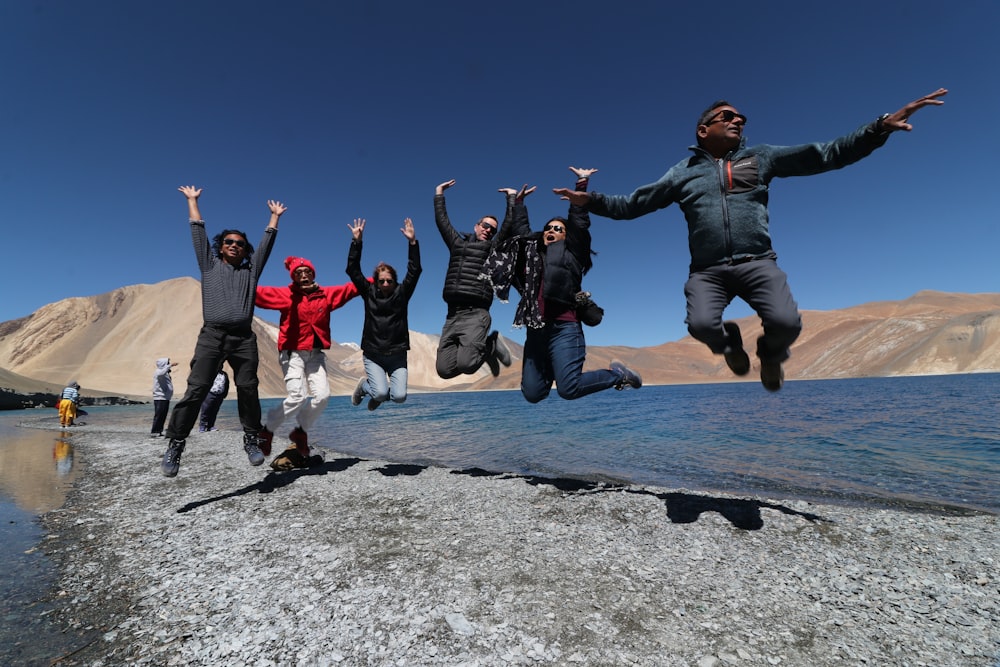 group of people jumping on gray rocky mountain during daytime