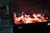 A warm, inviting shot of the smoke-filled barbecue pit at dusk, with glowing charcoal and flickering flames.
