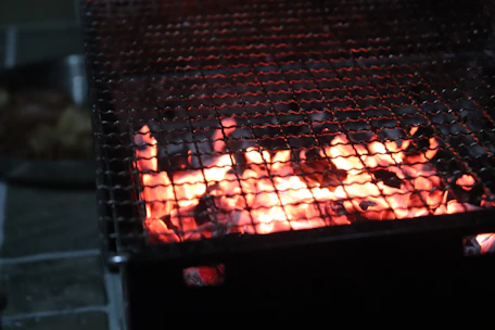 Close-up of fire flames licking the edges of a sizzling BBQ grill on a vintage ambassador setup.