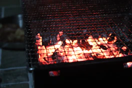 A warm, inviting shot of the smoke-filled barbecue pit at dusk, with glowing charcoal and flickering flames.