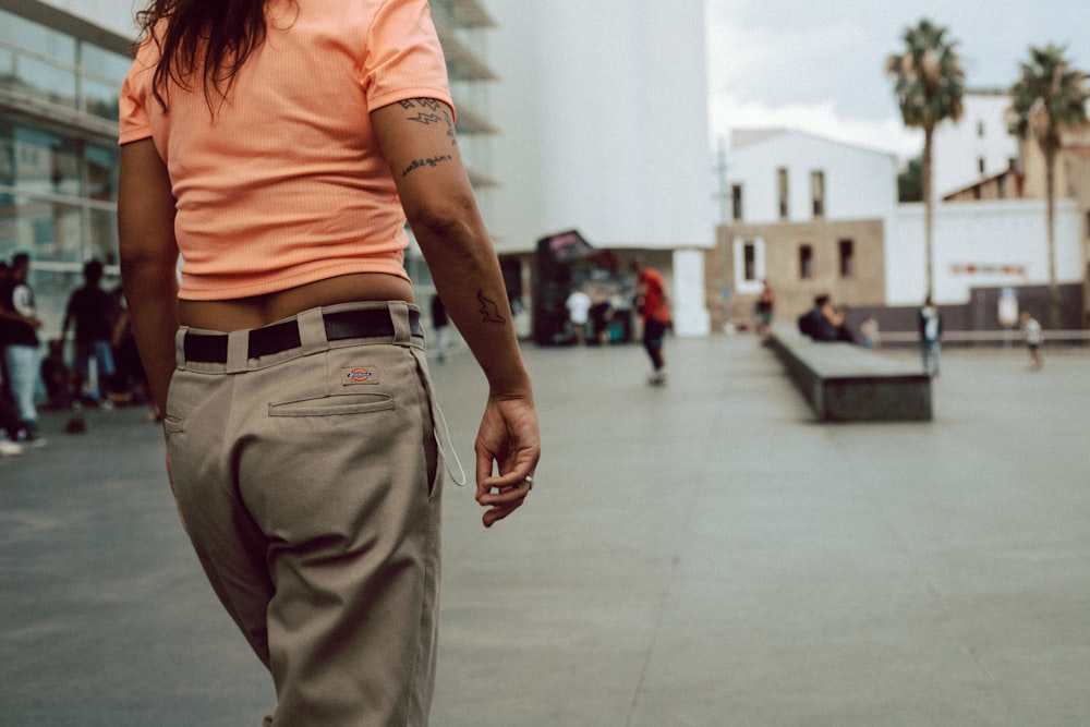 Frau in orangefarbenem T-Shirt und grauer Hose geht tagsüber auf dem Bürgersteig