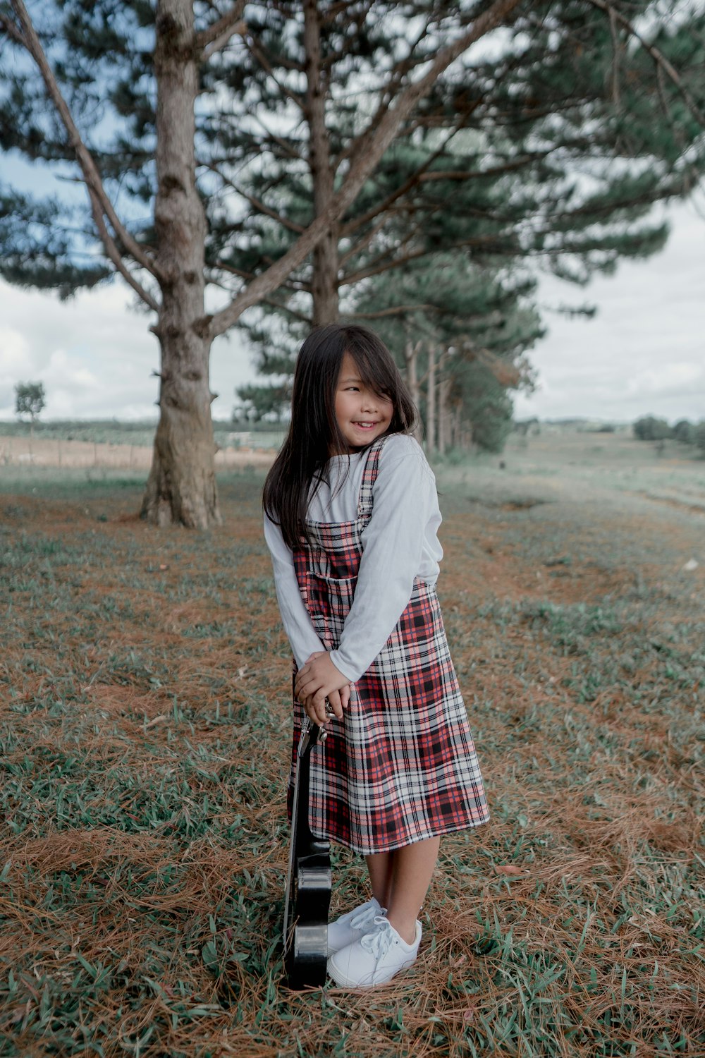 woman in white long sleeve shirt and red and black plaid skirt standing on green grass