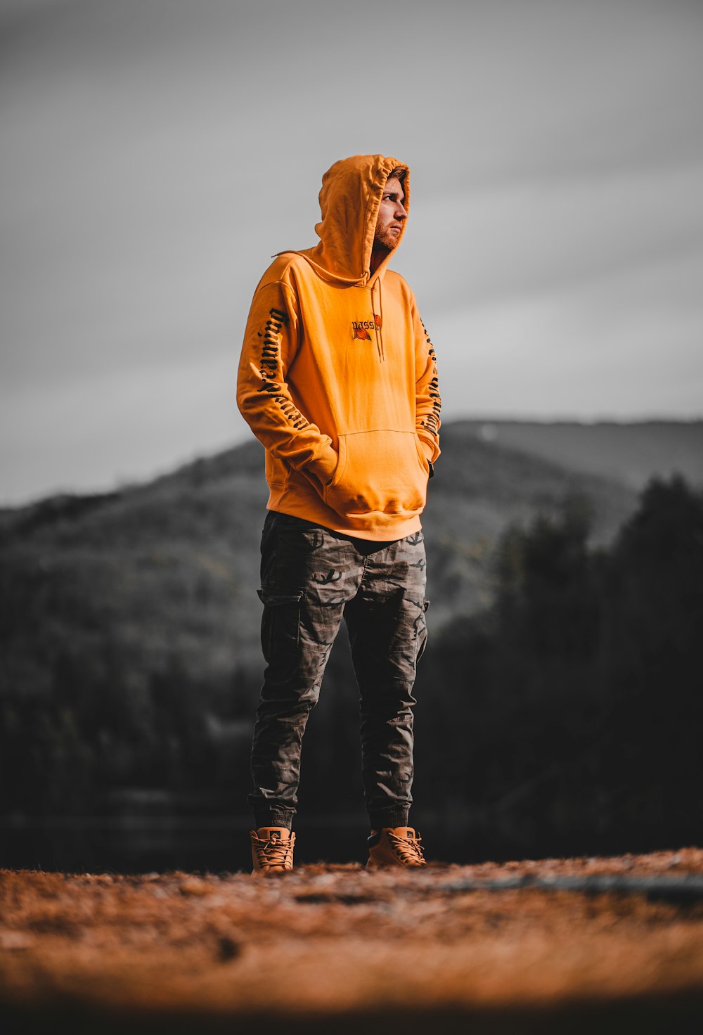 Mann in orangefarbenem Kapuzenpulli, der tagsüber auf Felsen in der Nähe eines Gewässers steht