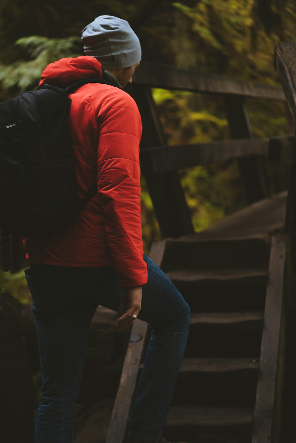 man in red jacket and blue denim jeans standing on wooden bridge