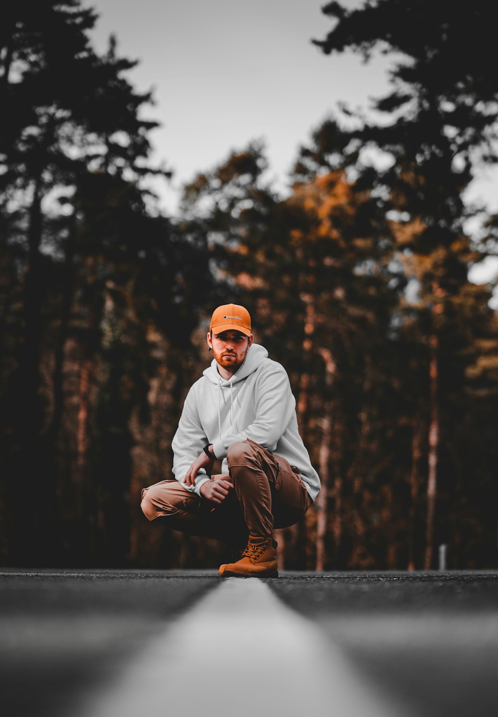 Hombre en sudadera con capucha blanca sentado en la cerca de madera marrón durante el día