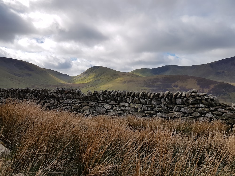 brown grass field near mountain under white clouds during daytime