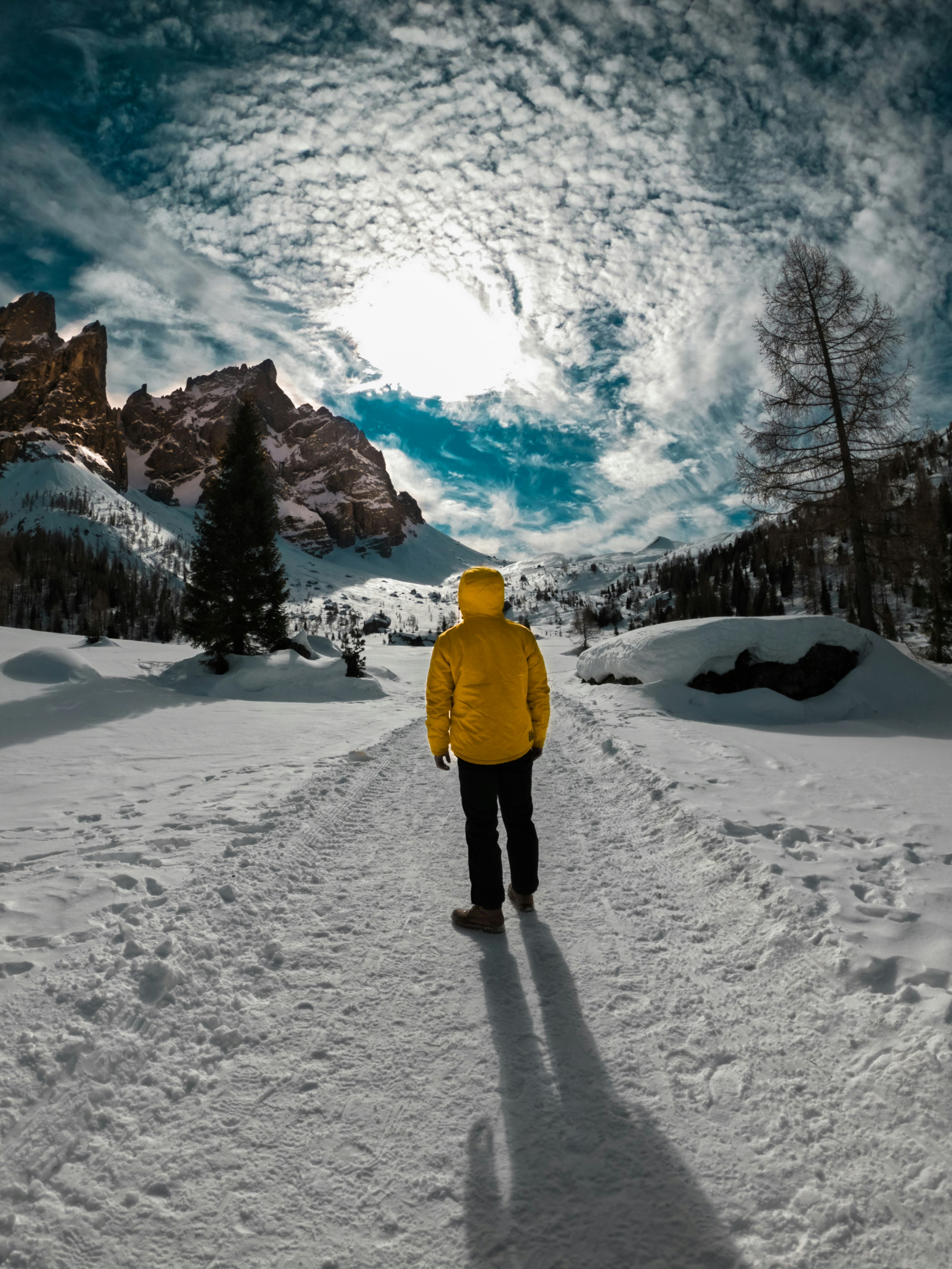 person in yellow jacket and black pants walking on snow covered ground during daytime
