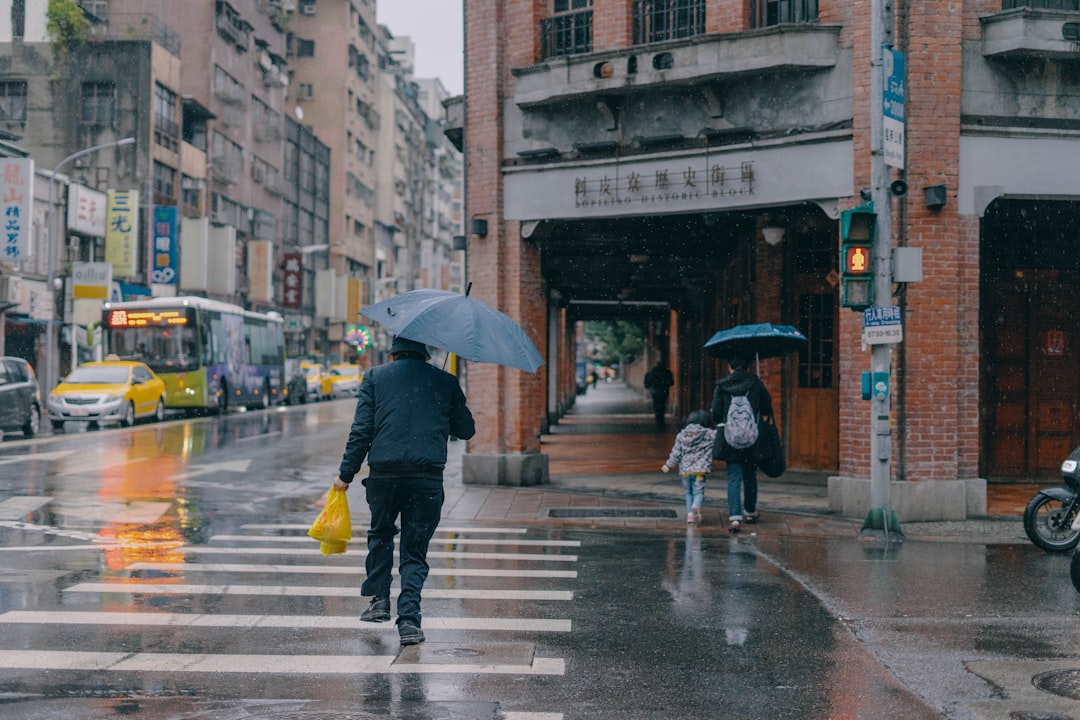 person in black jacket and yellow pants holding umbrella walking on pedestrian lane during daytime