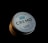 A round tin container prominently labeled 'CREMO' with additional text describing it as 'Barber Grade' and 'Sea Salt Texture.' The lid features a simplistic graphic of a crown and lists characteristics such as 'Low Hold' and 'Low Shine.' The container is partially illuminated against a dark background, creating a dramatic and focused presentation.