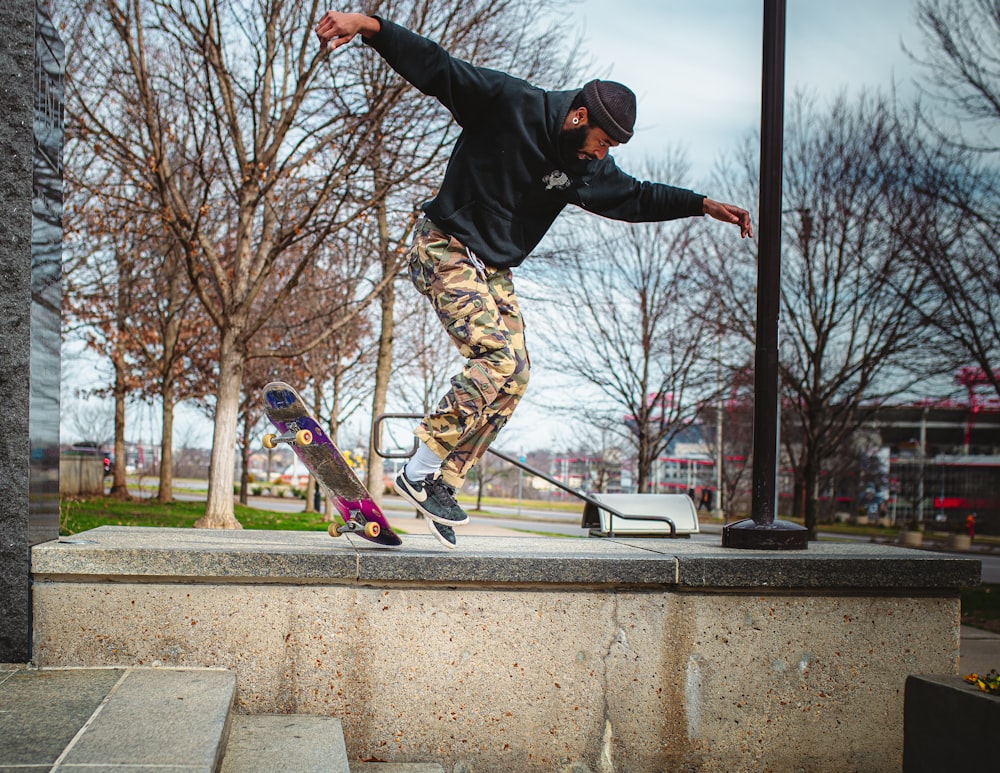 Uomo in giacca nera e pantaloni marroni che salta sullo skateboard durante il giorno