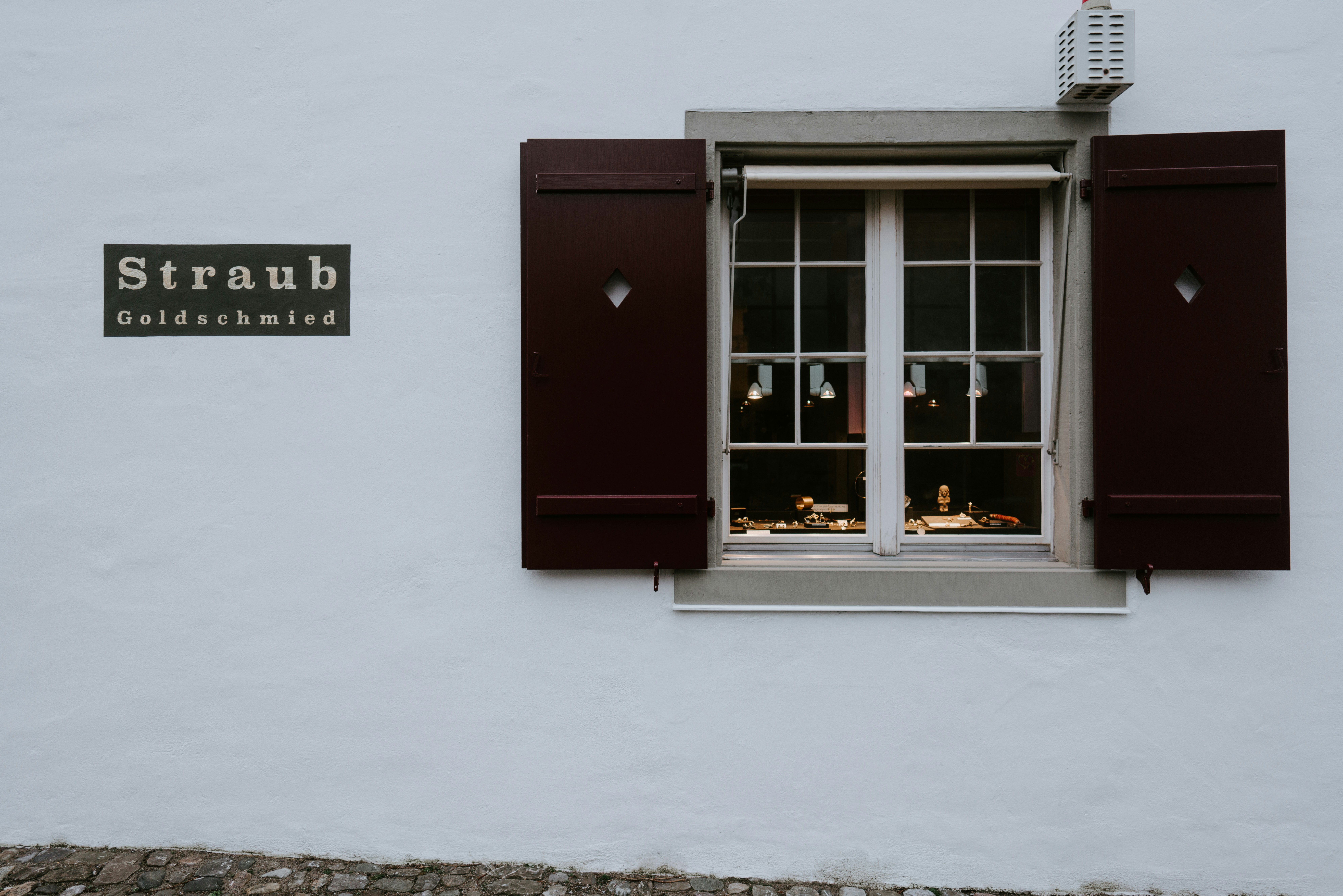 Straub Goldschmied shop window displaying jewelry on a white wall.