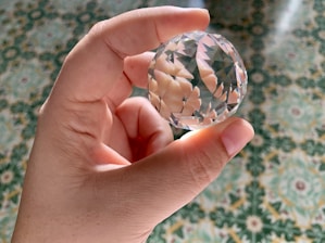 Close-up of hands delicately holding a crystal sphere over a geometric spiritual pattern.