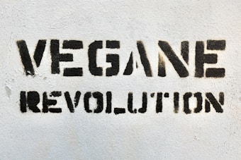 Bold black stencil text reading 'VEGANE REVOLUTION' is spray-painted on a textured white wall.