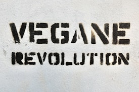 Bold black stencil text reading 'VEGANE REVOLUTION' is spray-painted on a textured white wall.