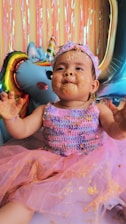 A cheerful toddler blowing out birthday candles surrounded by colorful balloons.