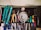 A collection of various hand tools neatly arranged on a black surface. The tools include pliers, screwdrivers, cutters, and a saw with handles in different colors such as turquoise, red, yellow, and green. A round metallic object is centrally placed, possibly a weight or industrial component. The tools appear well-used, hinting at a workshop environment. Below the surface, additional tools and a pair of blue gloves can be observed.