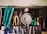 A collection of various hand tools neatly arranged on a black surface. The tools include pliers, screwdrivers, cutters, and a saw with handles in different colors such as turquoise, red, yellow, and green. A round metallic object is centrally placed, possibly a weight or industrial component. The tools appear well-used, hinting at a workshop environment. Below the surface, additional tools and a pair of blue gloves can be observed.