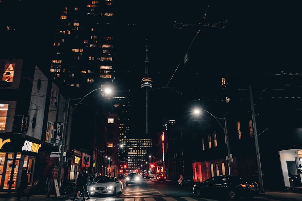 cars on road between high rise buildings during night time