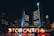 A nighttime cityscape highlighted by illuminated letters spelling out 'Toronto' in front of a modern building, with a mix of people walking around. The background features tall, brightly lit skyscrapers, contributing to the lively urban atmosphere.