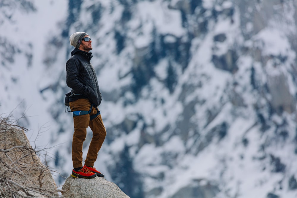 man in black jacket and brown pants standing on rock mountain during daytime