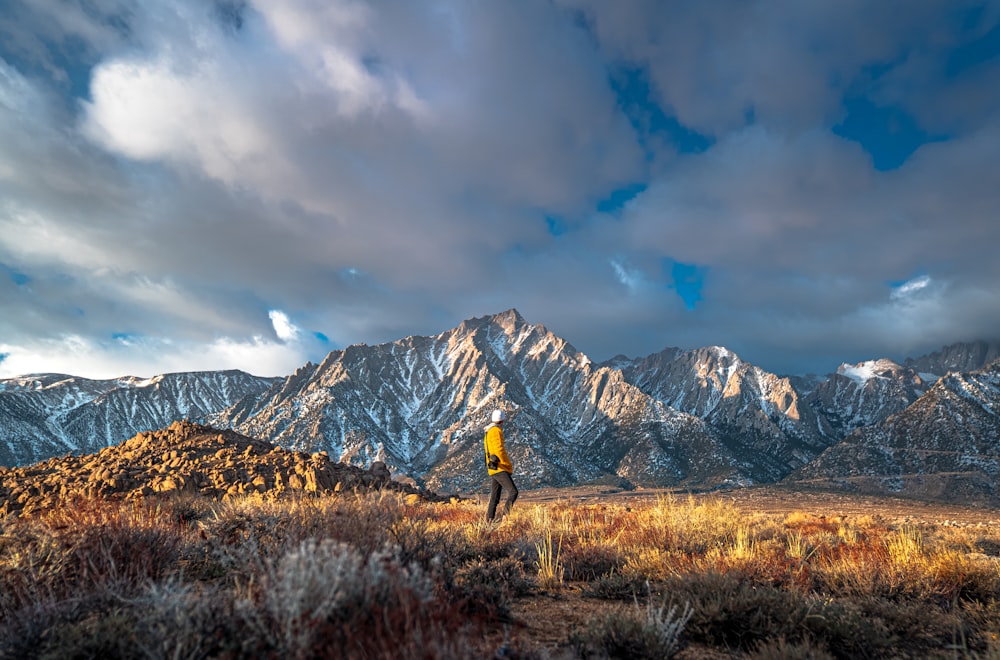 person in black jacket standing on brown grass field near snow covered mountain during daytime