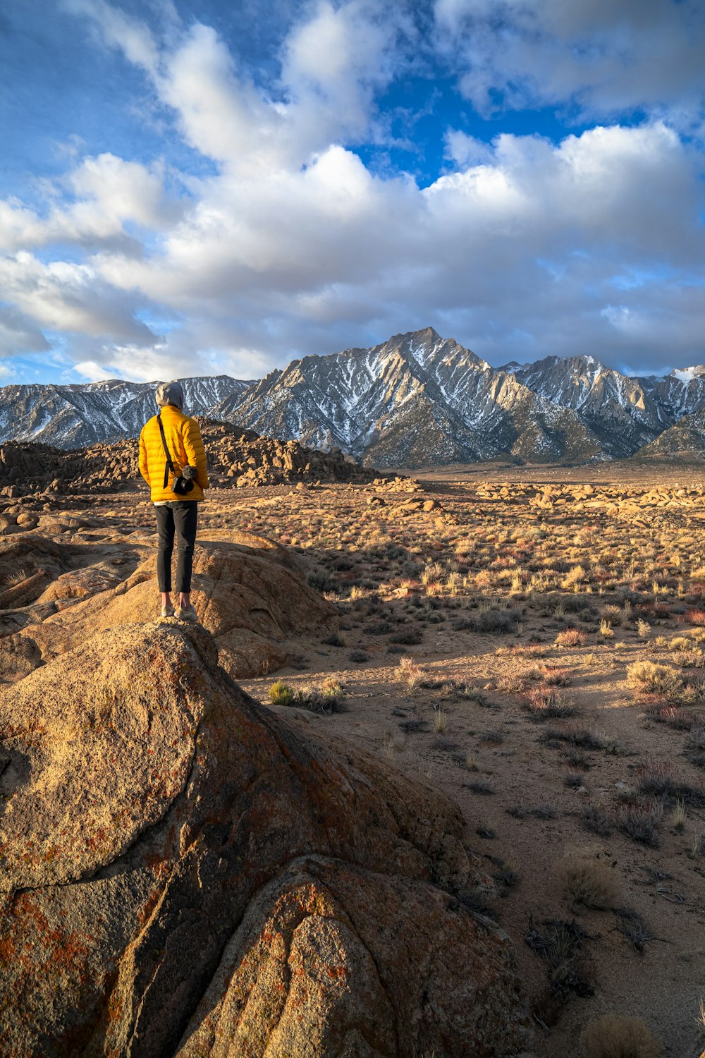 man in yellow jacket standing on brown rock during daytime