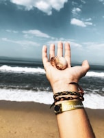 A hand holding a string of polished sea glass bracelets with the Okinawa coastline visible in the distance.