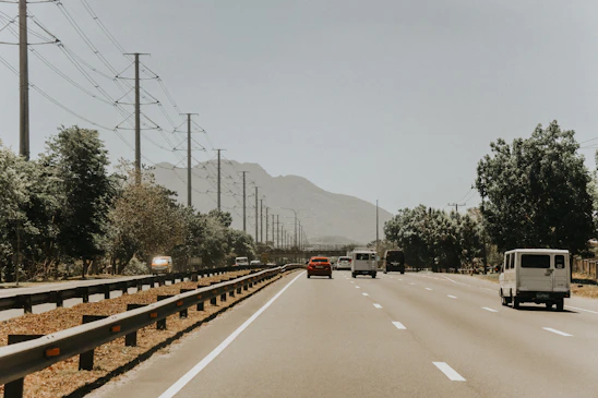 A modern car carrier loaded with vehicles driving along a highway under a clear blue sky.